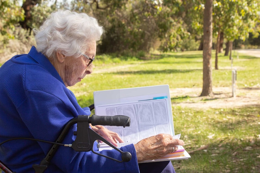 An elderly lady reads letters on a park bench on a sunny day