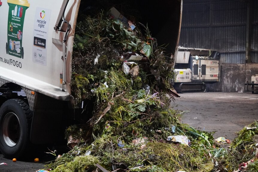 A truck is unlaoding organic matter with food scraps from the back of its open loading window