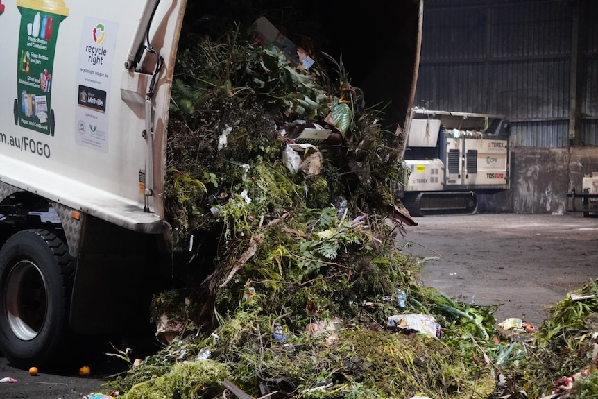 A truck is unlaoding organic matter with food scraps from the back of its open loading window