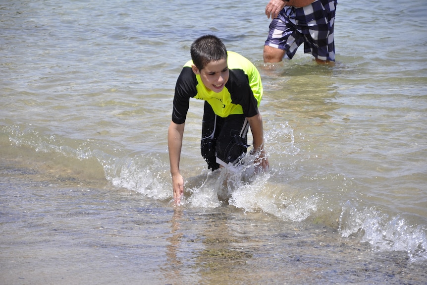 A young boy smiling and playing in the surf