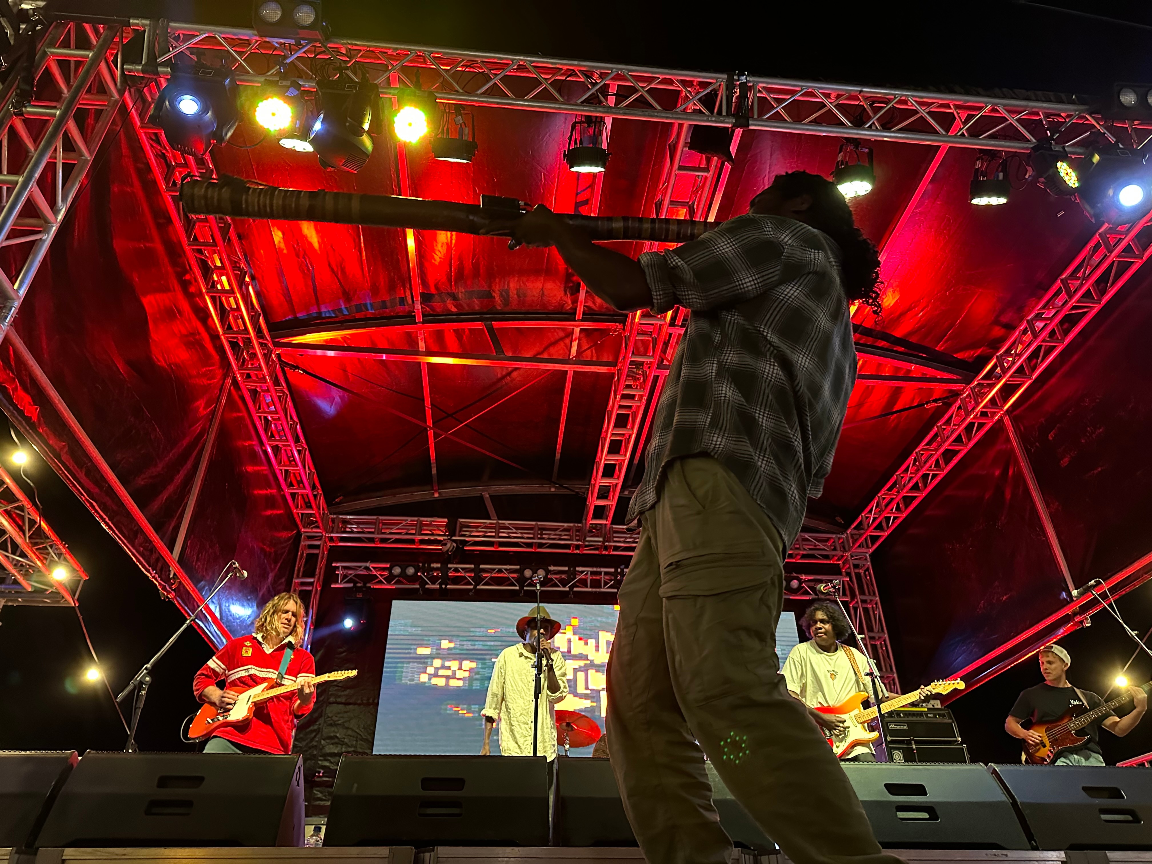 A man plays a didgeridoo on stage. 