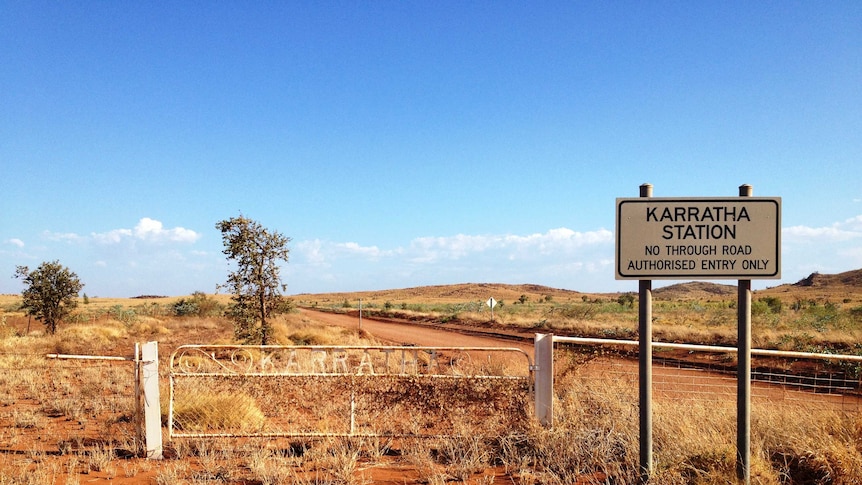Sun shines on Karratha Station's white entrance gate, which is surrounded by dry spinifex and red dust.