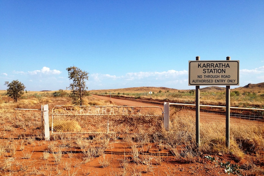 Sun shines on Karratha Station's white entrance gate, which is surrounded by dry spinifex and red dust.