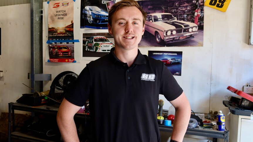A young race car driver in a shed, with car posters.