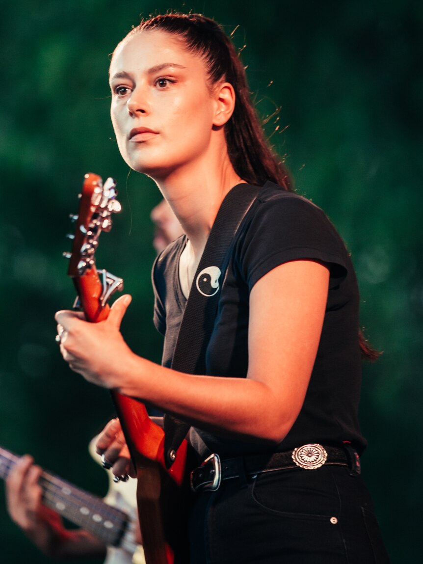 A woman in a black top plays guitar on stage and looks out to the crowd