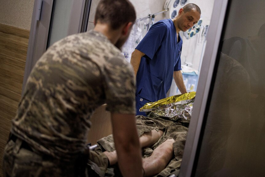 Lekarz i oficer wojskowy podnoszą nosze i trzymają przy drzwiach mężczyznę w wojskowym mundurze 