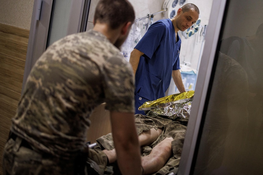 Ein Arzt und ein Armeeoffizier heben eine Trage mit einem Mann in Uniform durch eine Tür 