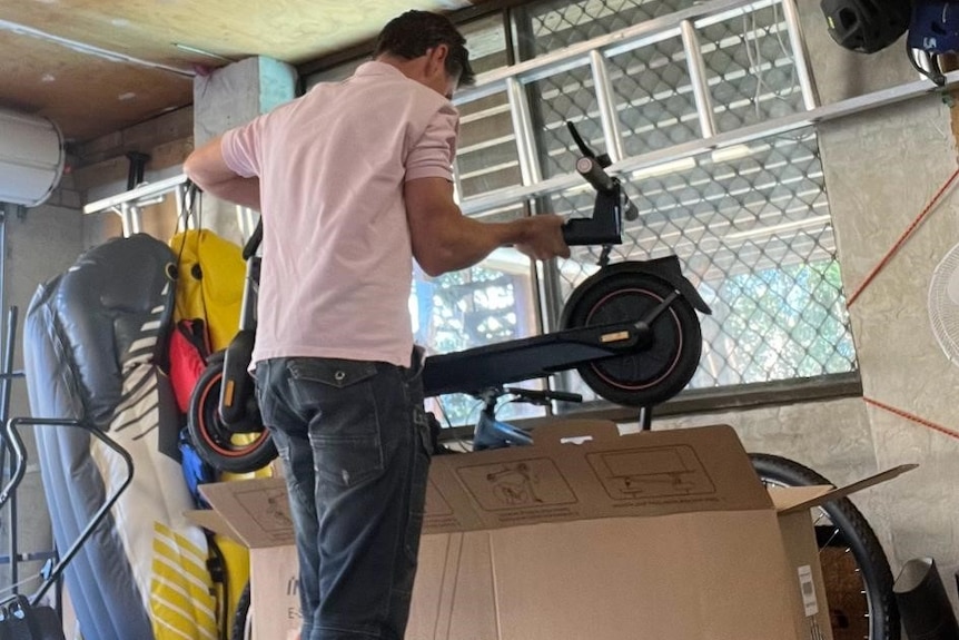 A man packs away an e-scooter into a cardboard box