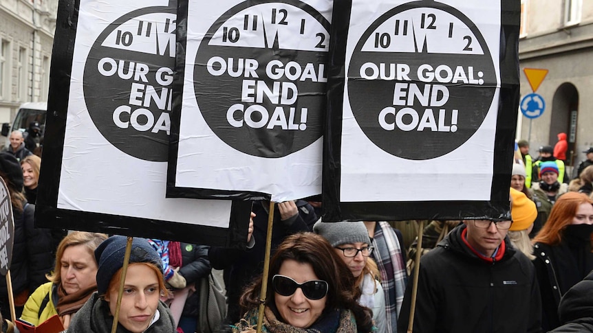 People hold three identical signs, with pictures of a clock ticking towards 12, and "Our goal: End coal!"