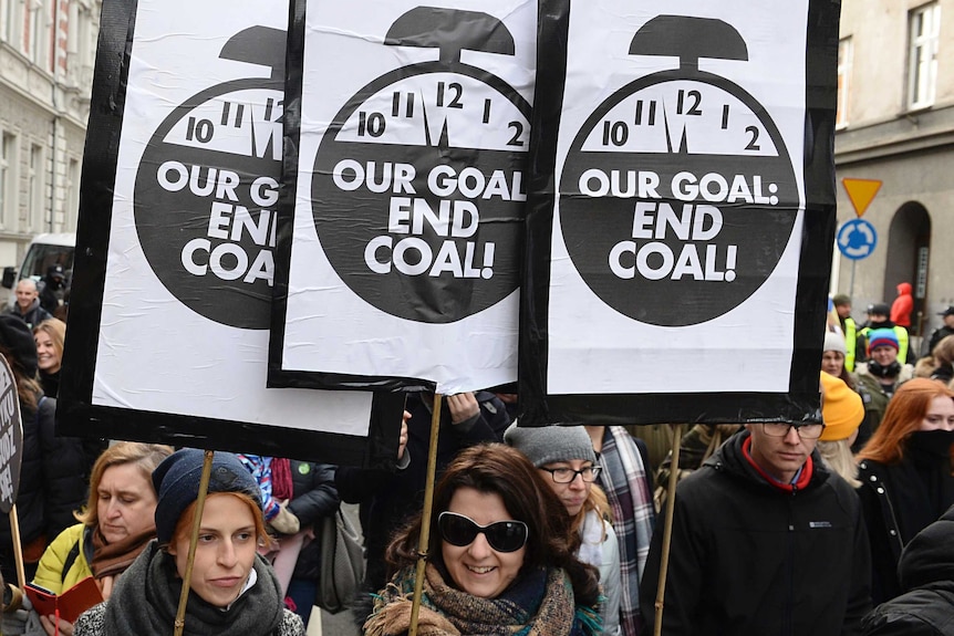 People hold three identical signs, with pictures of a clock ticking towards 12, and "Our goal: End coal!"