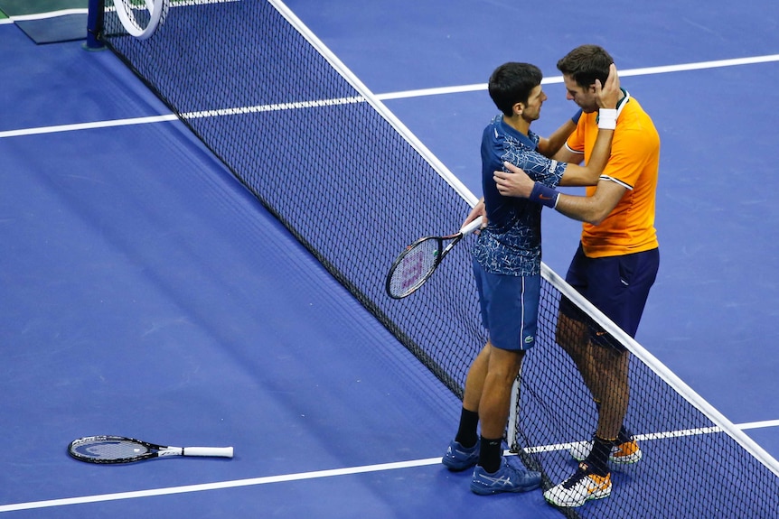 Two men embrace from either side of a tennis net
