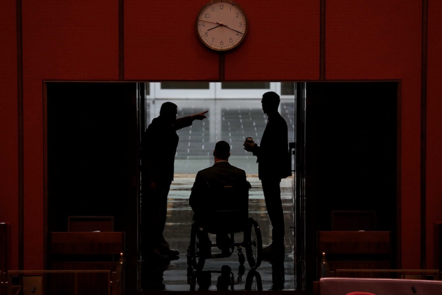 Silhouettes of Jordon Steele-John and two others are visible at the exit door to the Senate. A clock sits above the doorframe.
