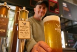 a man smiles and hands a beer over from behind a bar
