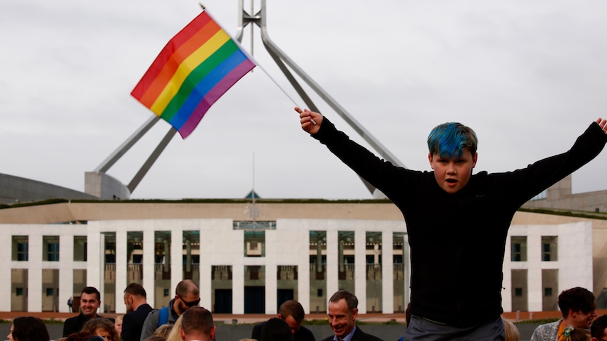 A boy waves a rainbow flag outside Parliament House.