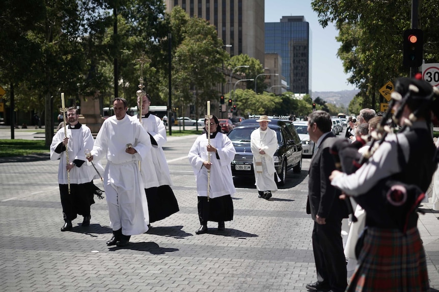 A man plays the bagpipes as a funeral procession walks through Adelaide's CBD