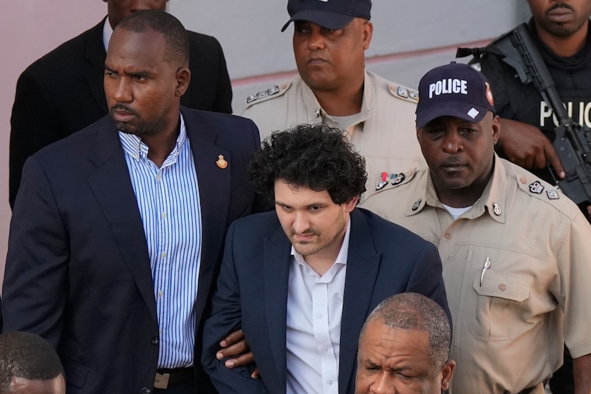 A man in a suit is escorted by police from a courthouse.