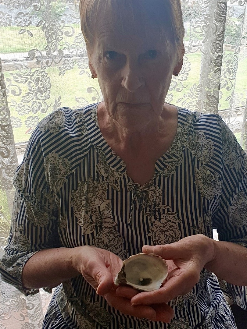 A woman holding a oyster shell with a pearl in it.