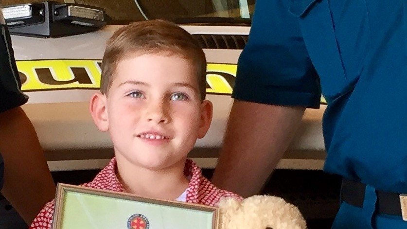 Five year old boy stands smiling with certificate and teddy bear.