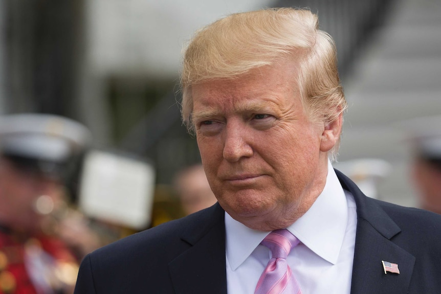 Wearing a black suit, pink tie and US flag pin, Donald Trump looks to the left across the shot