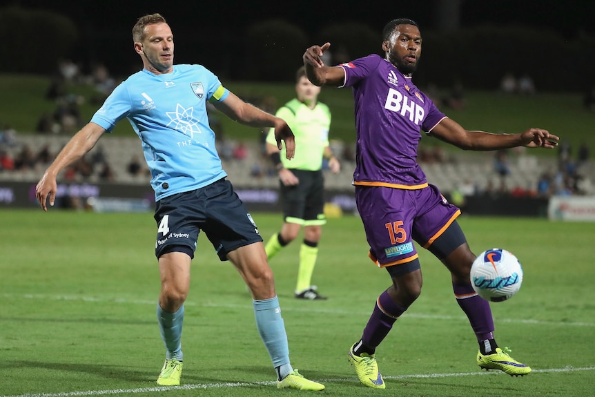 Alex Wilkinson and Daniel Sturrindge lean out for a soccer ball during a march between Sydney FC and Perth Glory
