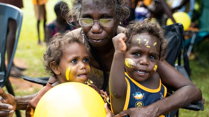 Two young fans with face paint and one older woman at the Tiwi grand final.