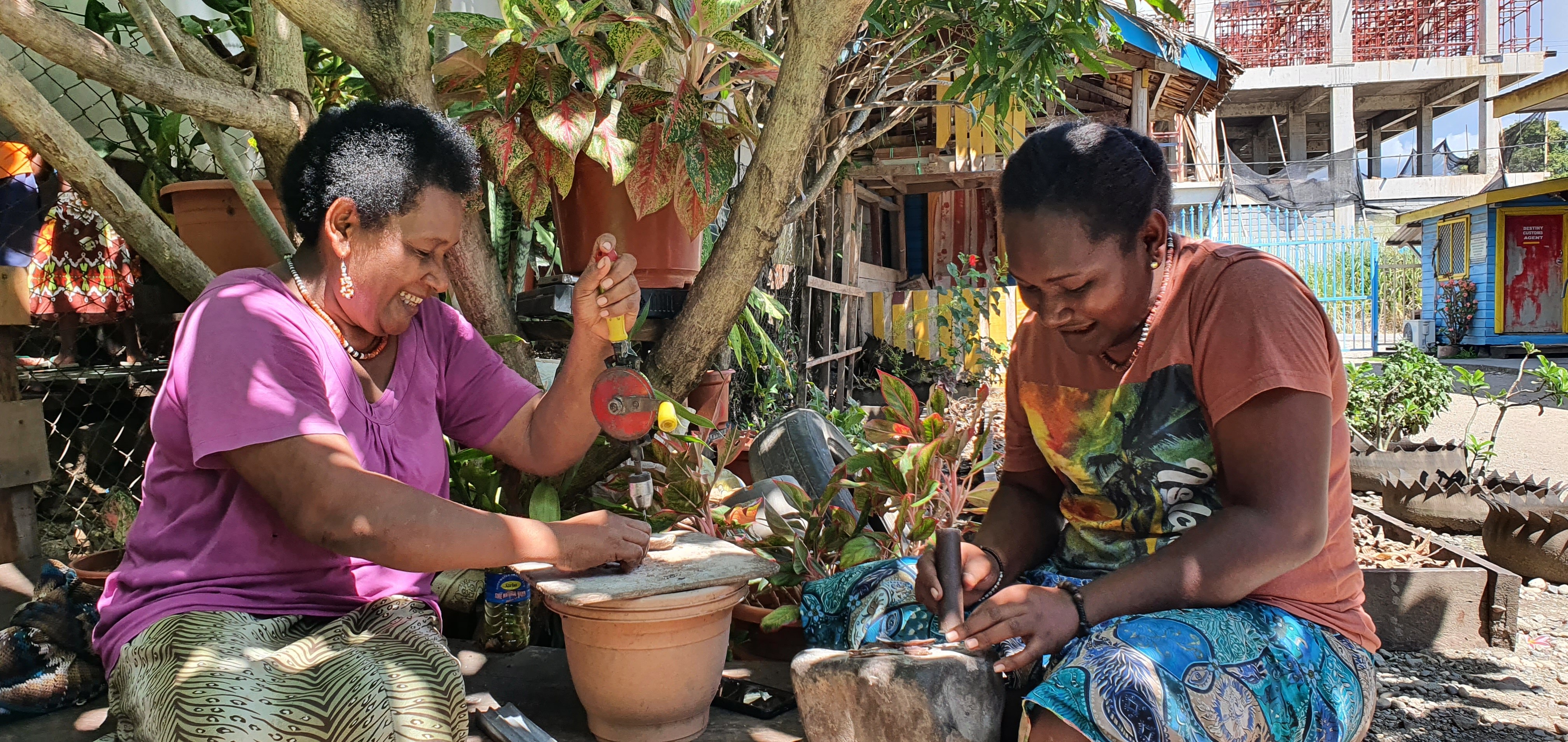 A mother and daughter sit outside.  The two women are grinding and drilling shells.