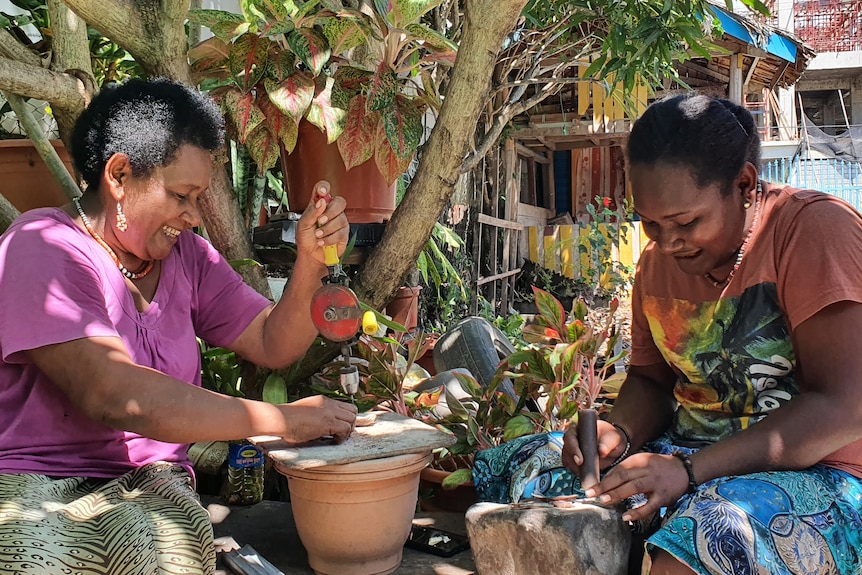 A mother and daughter sit outside. The two women are grinding and drilling shells.