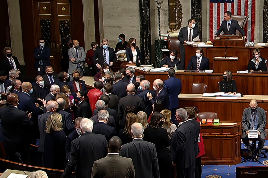 People mill around on the floor of the House.