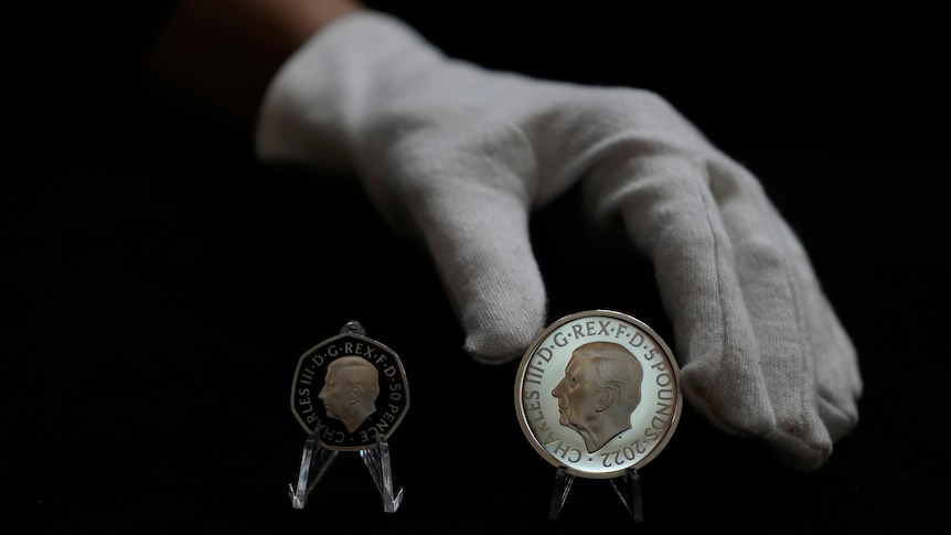 white glove hand places commemorative coin besides a smaller, black one