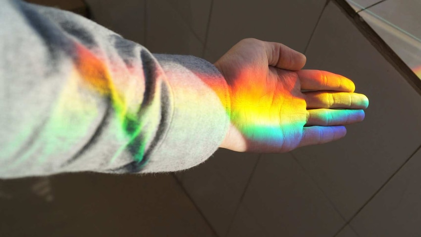 Hand with rainbow light reflecting on it for list of queer and LGBTIQ support numbers and websites in Australia