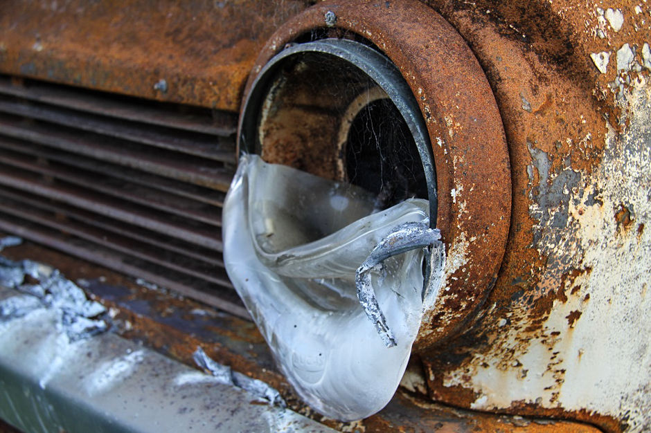 Detail photo of an old car's headlight with the glass melted and the metalwork heavily rusted.