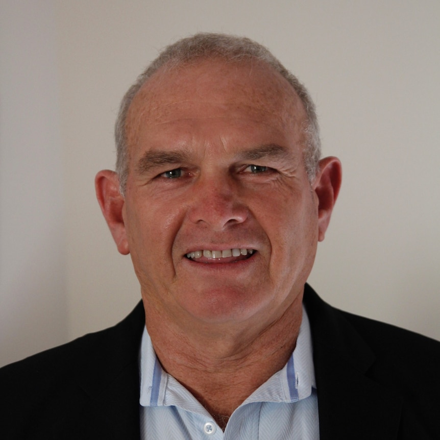 A man in shirt and blazer smiles.