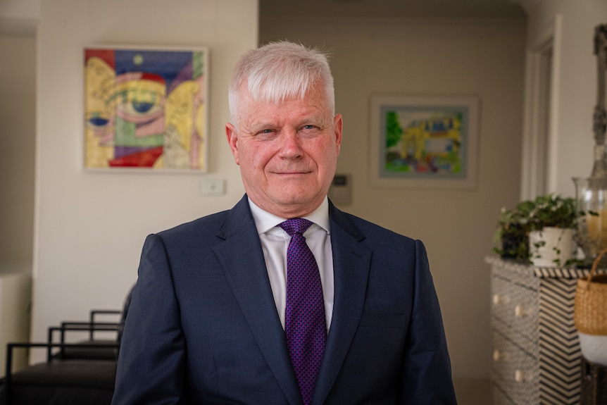 An older man with grey hair wearing a suit and tie with a purple tie.