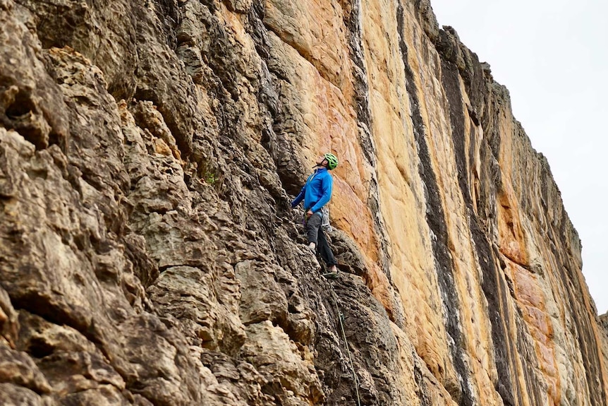 A man in a helmet climbs a sheer rock face with a rope and climbing gear