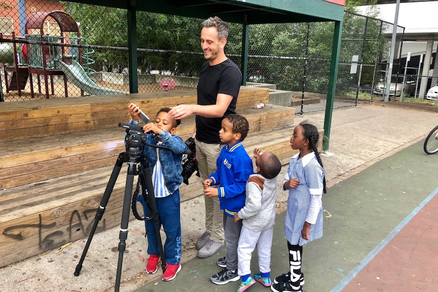 Children looking at tripod and iphone with Mat Marsic holding camera watching on.