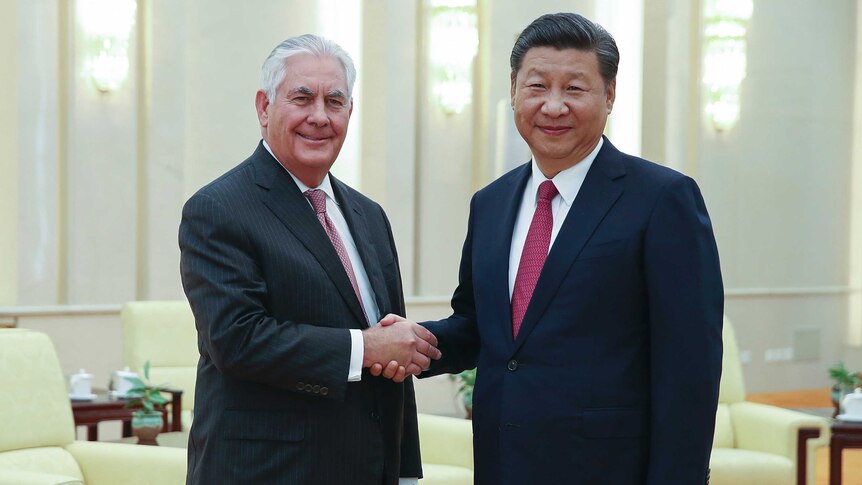 Rex Tillerson shakes hands with President Xi Jinping in China. They are both smiling looking into the camera.