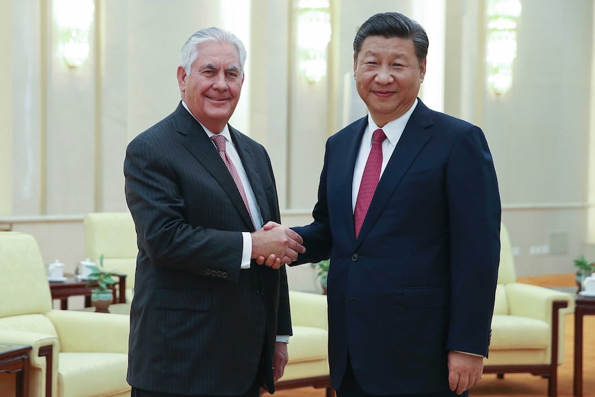 Rex Tillerson shakes hands with President Xi Jinping in China. They are both smiling looking into the camera.