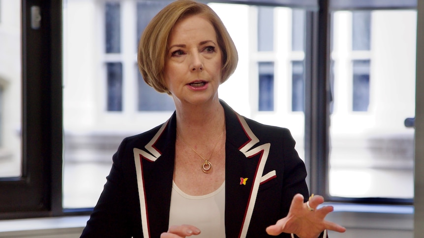 Julia Gillard sitting at a meeting table in a city office and speaking.