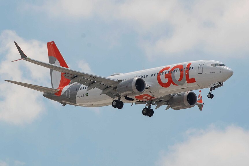 A airplane with orange and white livery descends in the air.