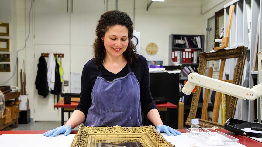 Holly stands looking at an ornate gold frame.
