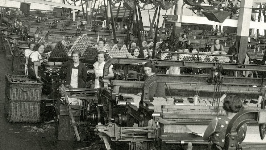 a black and white image inside an old weaving mill with women behind the machines