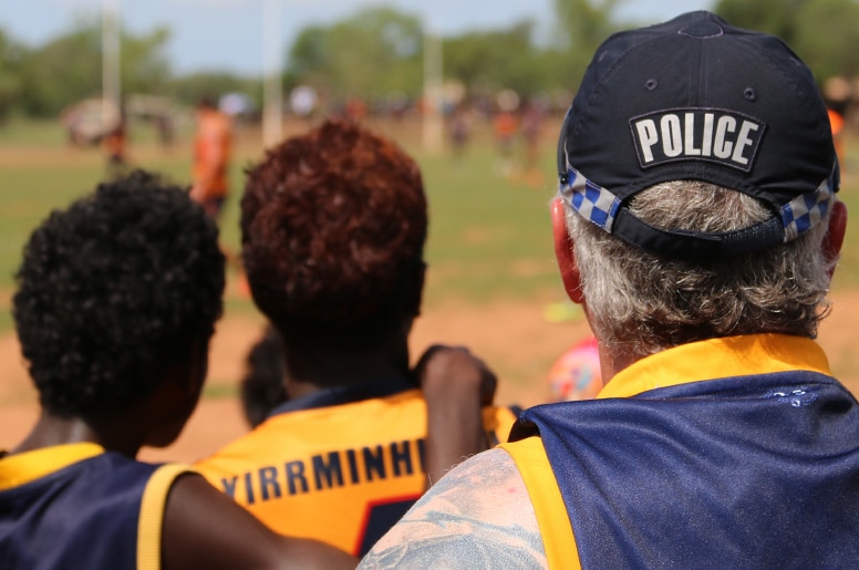 A police officer and two young men watch and AFL match.