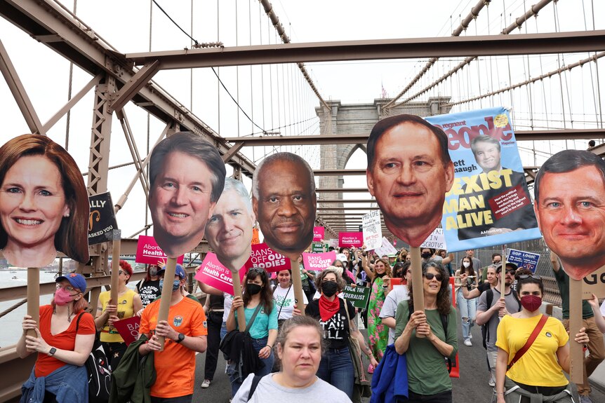 Protesters hold huge cardboard cut-outs of the heads of five US Supreme Court justices while marching on the Brooklyn Bridge