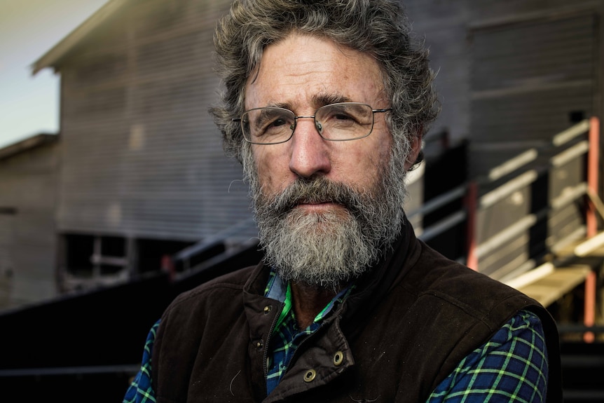 Un homme avec une barbe et des lunettes regarde directement la caméra.