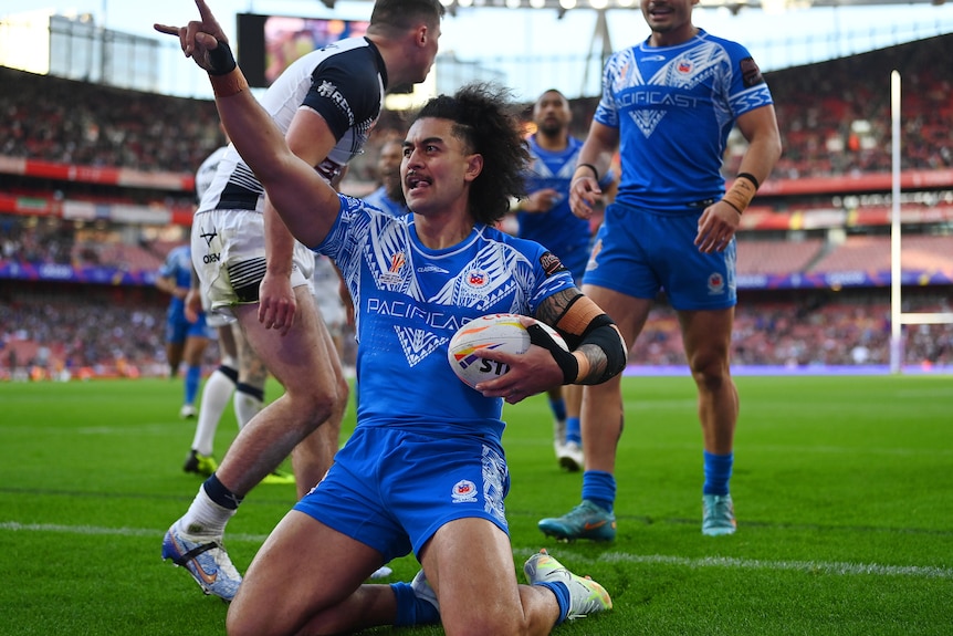 A man in blue salutes in the air after scoring a try.