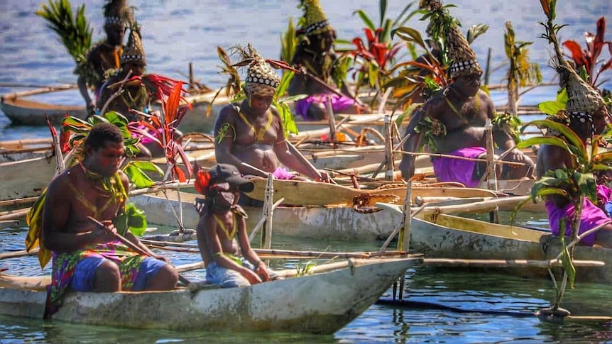 Men in traditional costumes in canoes on water.