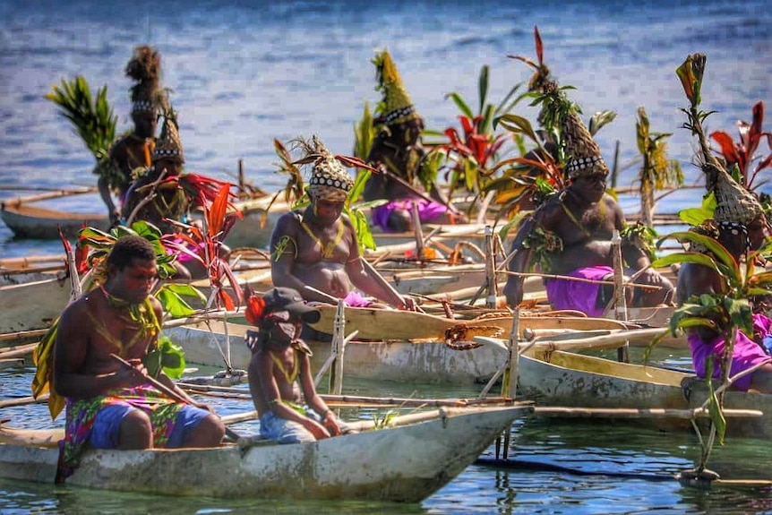 Men in traditional costumes in canoes on water.