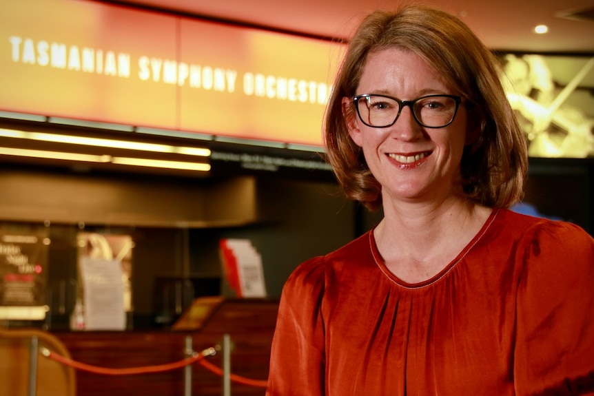A woman smiles in front of signage for the Tasmanian Symphony Orchestra