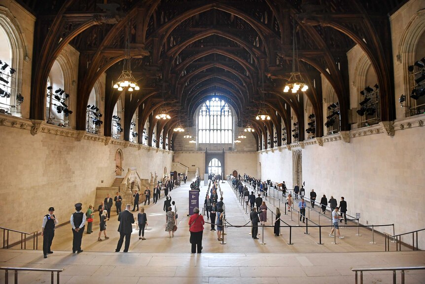 A large hall filled with a snaking queue of people all standing a couple of metres from one another.