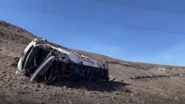 A bus lies mangled at the bottom of a hill.